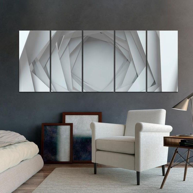 A modern living space featuring a white armchair next to a wooden side table with a lamp, in front of a dark gray wall adorned with a multi-panel art piece depicting abstract white geometric shapes.