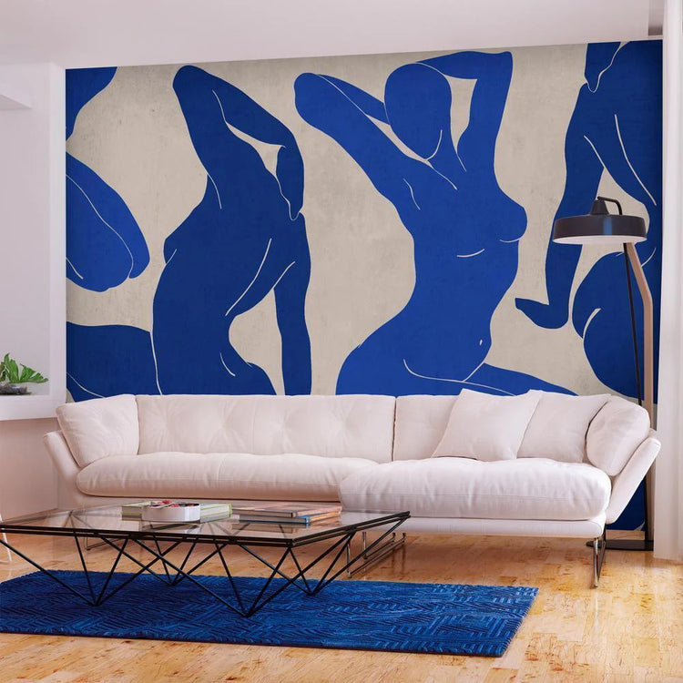 A modern living room featuring a white couch, blue rug, and a wooden coffee table with a geometric lamp, plus a wallpaper that features people in blue