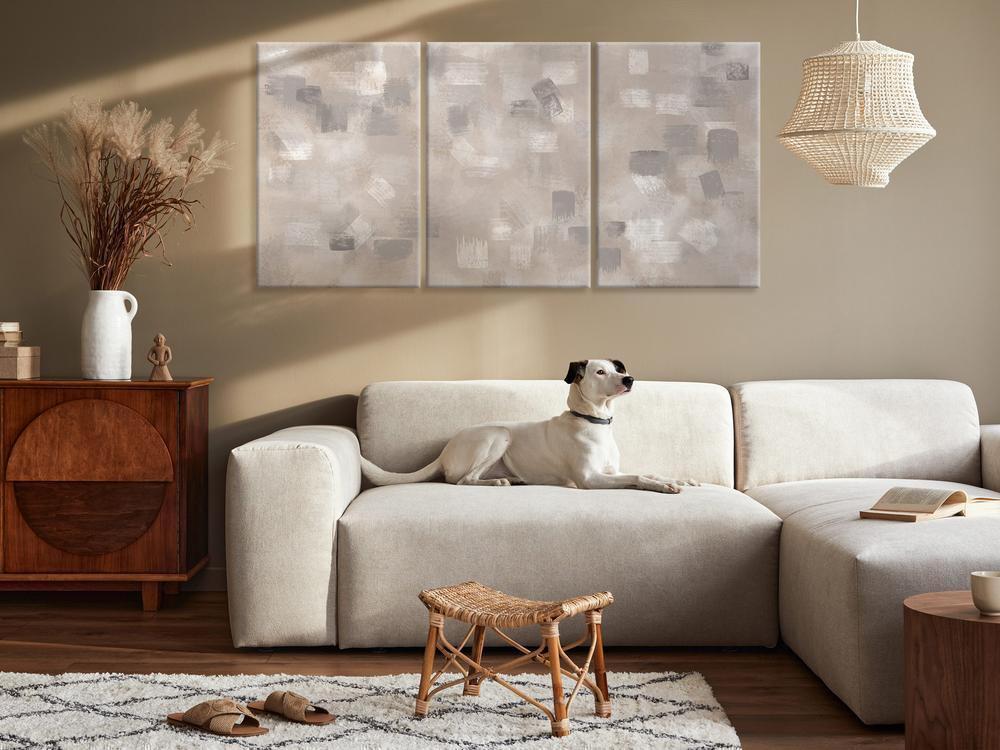 A modern living room features a large abstract canvas print in shades of blue and gray hanging above a white couch. Cute dog sitting on the couch