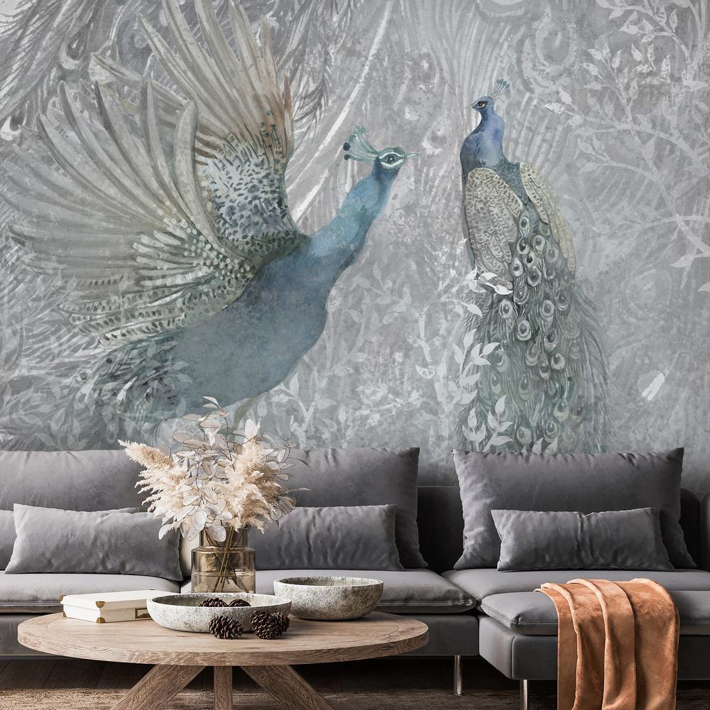 A modern living room featuring a brown leather couch, patterned rug, and a forest mural covering an accent wall. The mural depicts two peacocks dancing