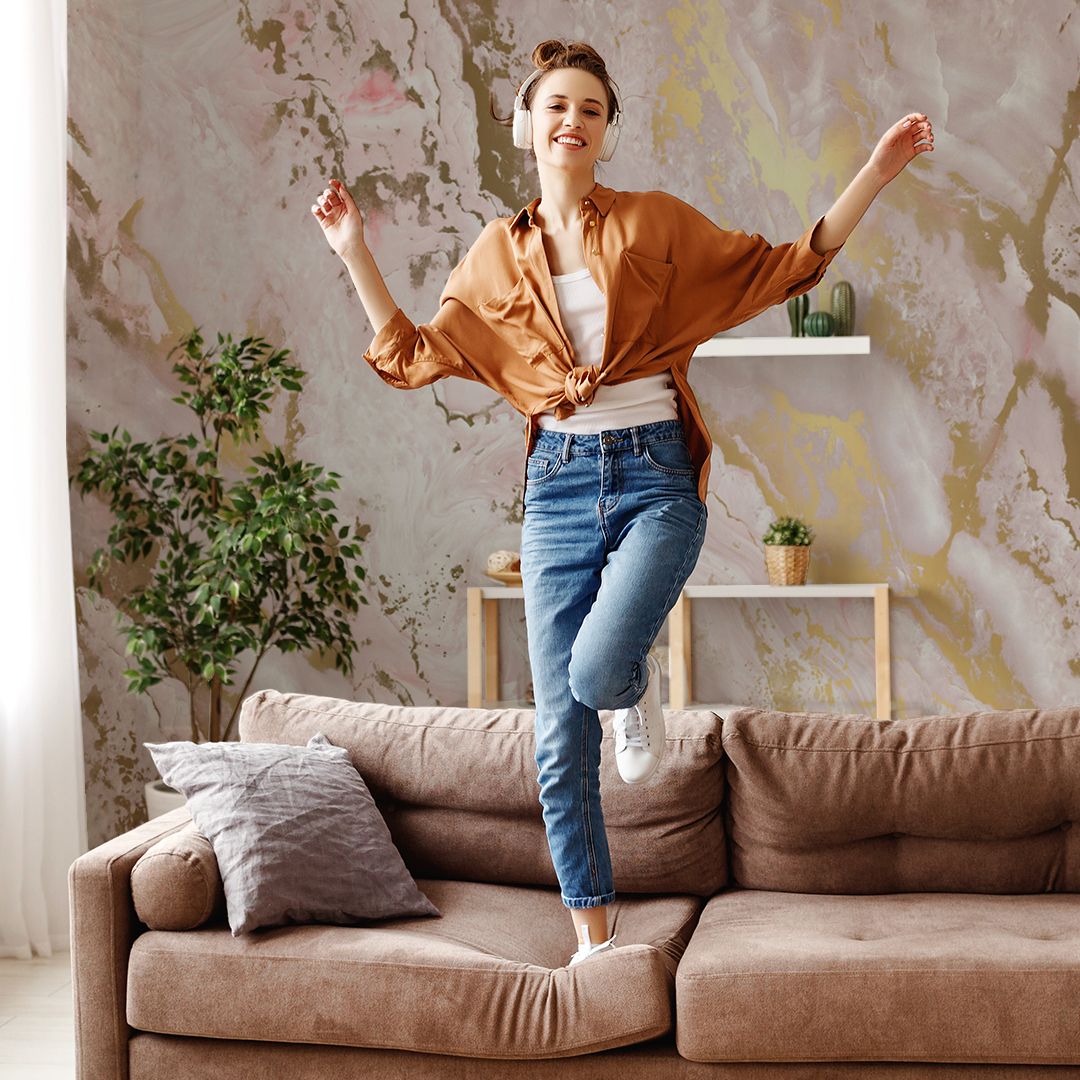 a woman standing on her sofa and she's very happy because she just finished mounting her beautiful patterned marbled and gold wallpaper to finish the look of her cosy and chic living room