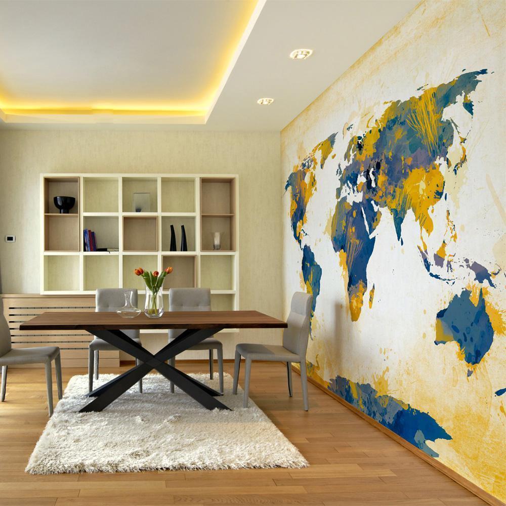 A cozy living room features a blue couch, patterned rug, and a world map mural covering an accent wall. The mural features oceans in blue and continents in various shades of green, yellow, and blue