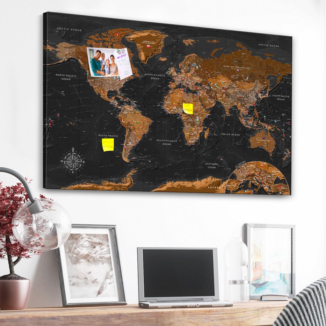 a cork pin board  on top of a desk with a world map in Black and brown design, you can also see some notes and an image pinned in the corkboard