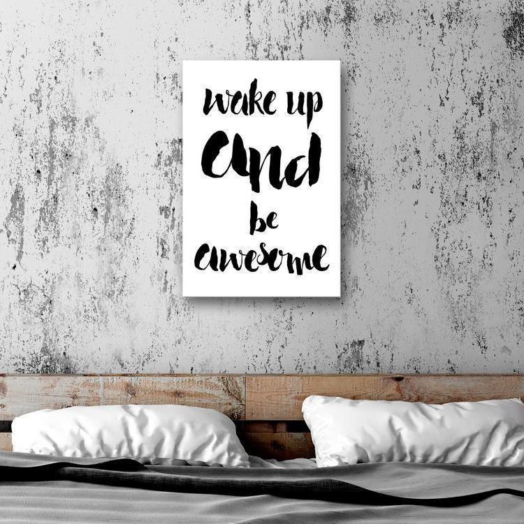 A black and white motivational poster that says "Wake up and be awesome" hangs above a black metal bed frame with white bedding.