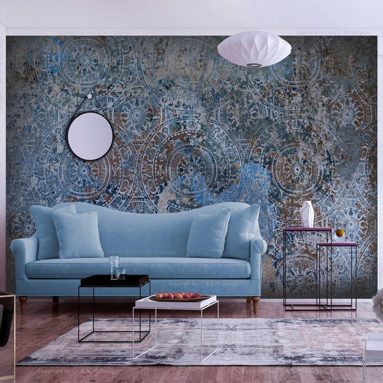 A blue couch sits in front of a wall with geometric wallpaper in shades of blue and brown