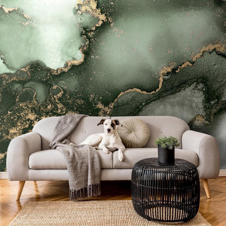 A dog sitting on a brown couch in a living room with green and gold marble mural wallpaper