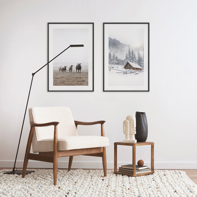 A living room with a mid-century modern armchair and a lamp. There are two poster frames on the wall behind the armchair displaying winter wall art
